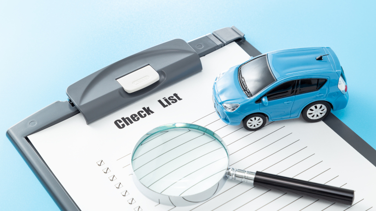チェックリストの上におもちゃのクルマと虫メガネのイメージ写真