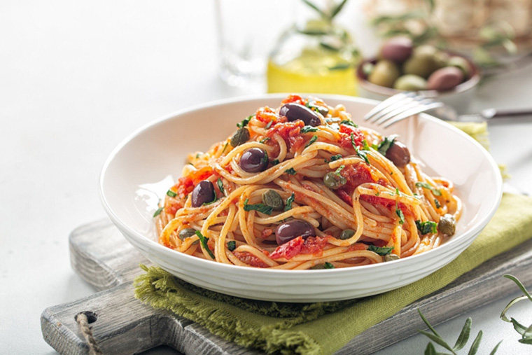 スパゲッティアッラプタネスカ - トマト、オリーブ、ケッパー、パセリとイタリアのパスタ料理。明るい背景。