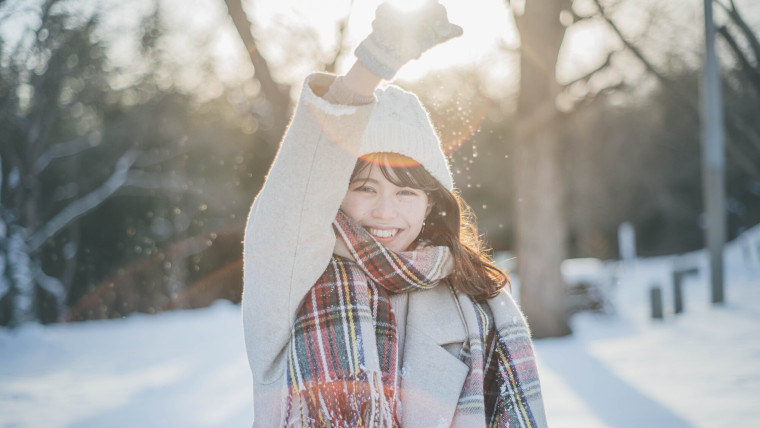 太陽の差し込む雪景色の中でほほ笑む女性