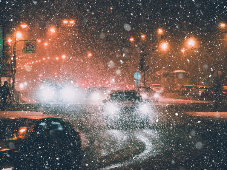 雪の振る夜、路面が黒く見える道路を走るクルマ