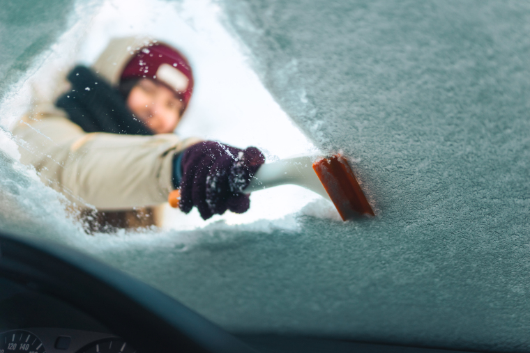 車のフロントガラスに付着した雪をアイススクレーパーで取り除こうとしている人