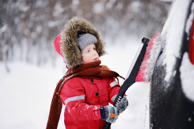 子どもがスノーブラシを使って、クルマに付着した雪を払おうとしている光景
