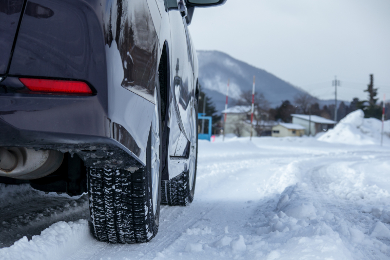 積雪のある路上に止まっているクルマの、リア側のタイヤや排気口、下回りの一部が見えている