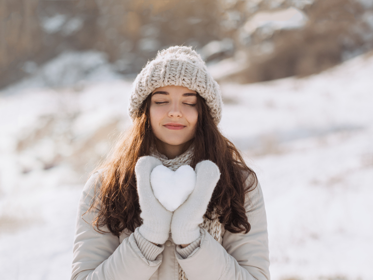雪の中、美しい女性が雪で作ったハート型を両手で持ち、優しい表情で佇んでいる