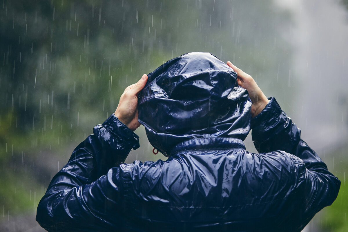 雨の中、レインジャケットのフードを被っている後ろ姿