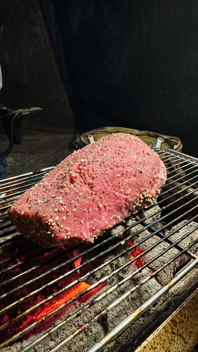 スパイスをまぶされ網の上で焼かれるかたまり肉の写真