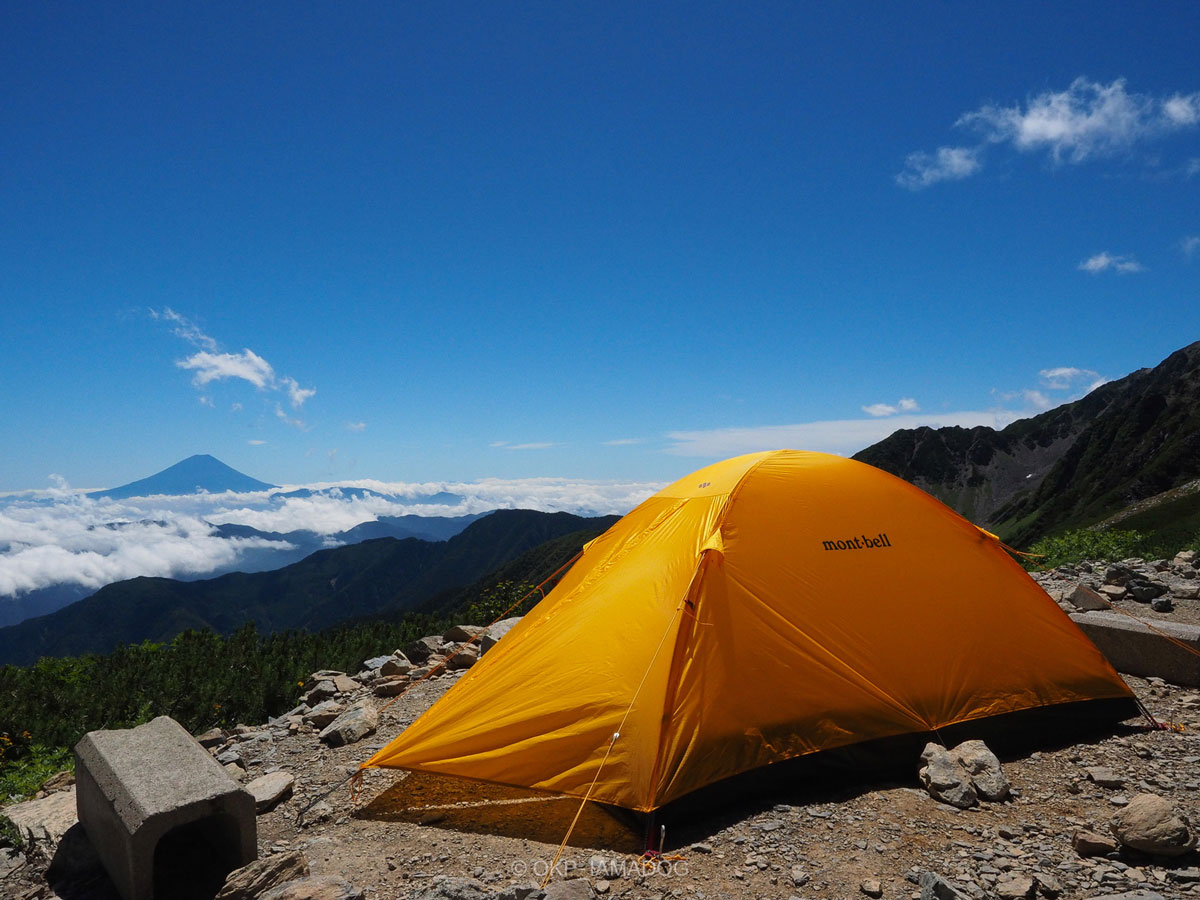 オレンジ色のモンベルの山岳テントの写真。青空の下、雲海の向こうに夏の富士山を望む。