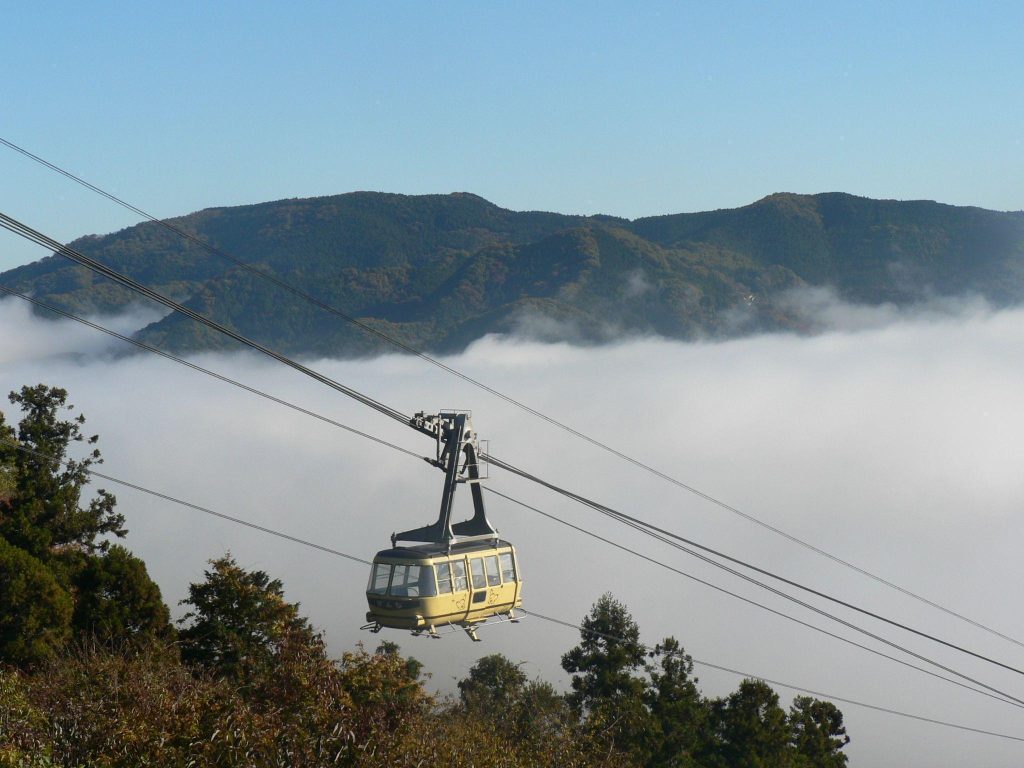 雲海の上を、黄色いロープウェイのゴンドラが山に向かって進んでいる。