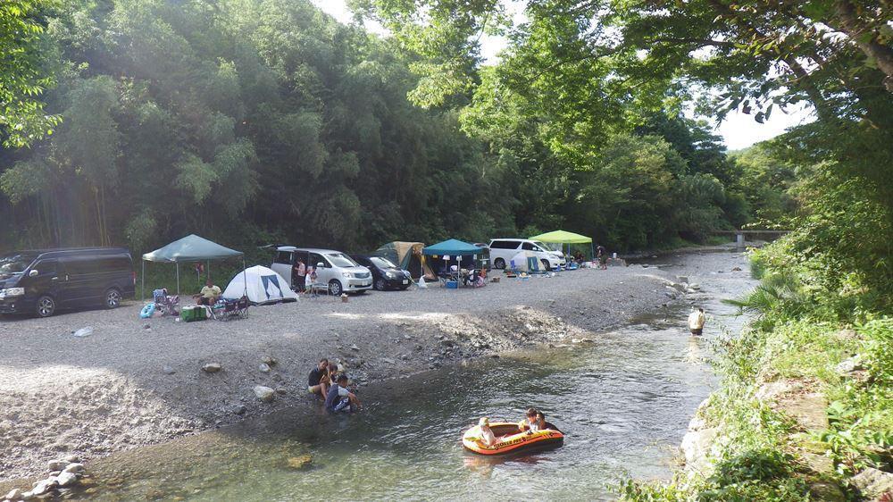 川原にテントや車が並び、川遊びを楽しむ家族がいる。