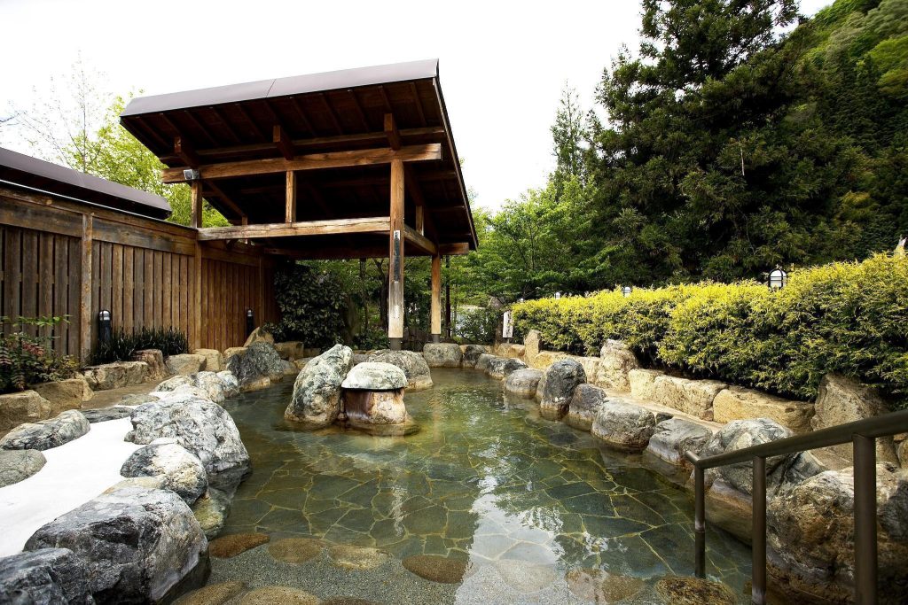 木々に囲まれた岩造りの露天風呂。屋根と手すりがある。