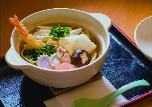 大きな器に入ったうどん。エビの天ぷら、椎茸、かまぼこ、焼き餅など様々な具材が乗っている。