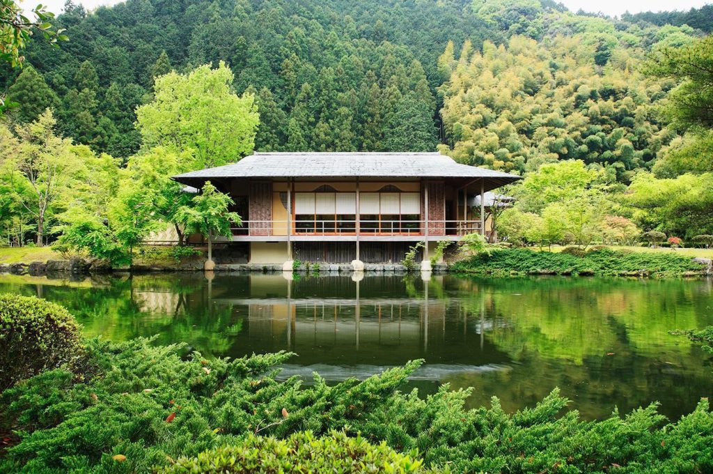 庭園の池に面して建つ、日本家屋。木々が水面に映っている。