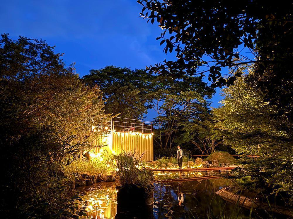 暗い夜にライトアップされた池。木製の橋と、その向こうには建物が見える。
