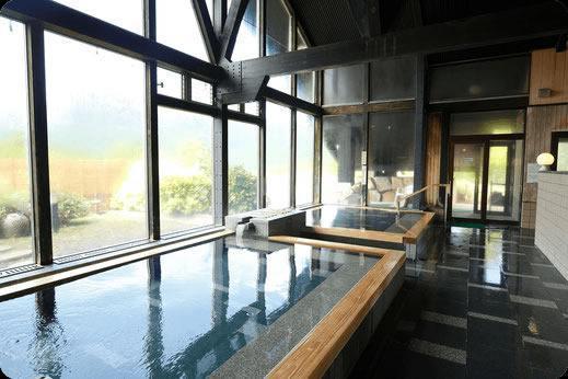 窓が大きく開放的な温泉の内湯。木枠と岩でできた湯船が2つある。