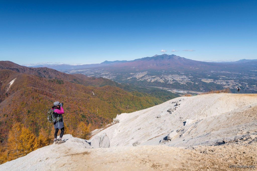 山頂から、壮大な山々と麓の街並みを眺める人物。
