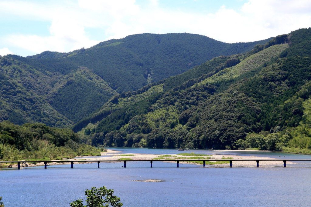 緑の山々に囲まれた広い川の上を、橋が架かっている。