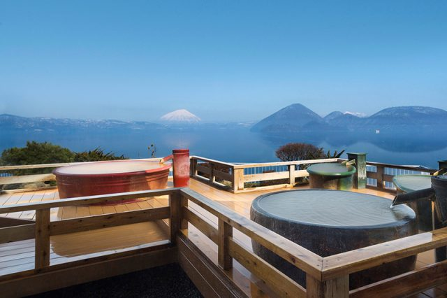 湖に面した木製の露天風呂のデッキ。遠くには雪をかぶった山々が見える。