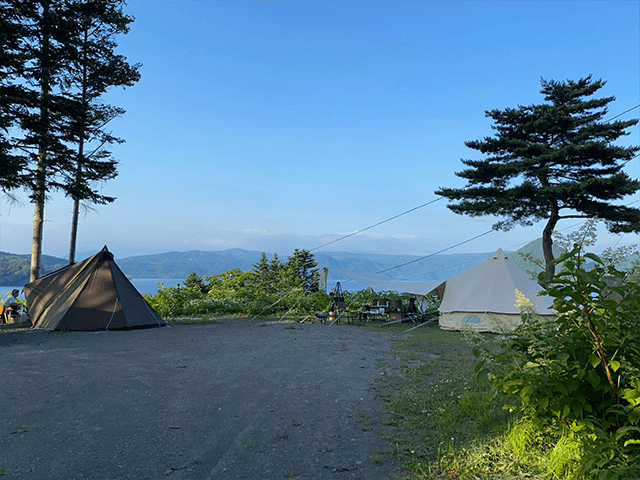 湖畔のキャンプ場。2つのテントが設営され、向こうには青い湖と山々が見える。
