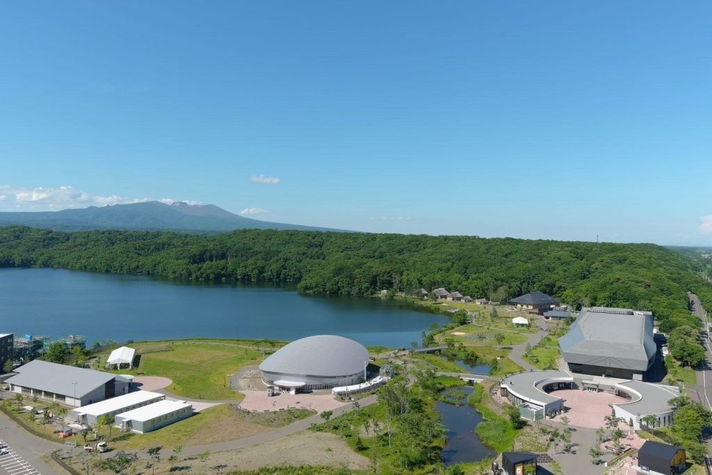 湖畔に建つ近代的な建物群の空撮。奥には山が見える。