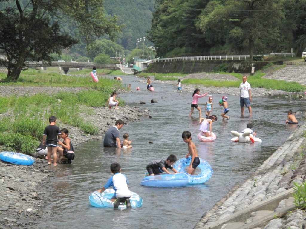 多くの家族や子供たちが、浅い川で水遊びを楽しんでいる。