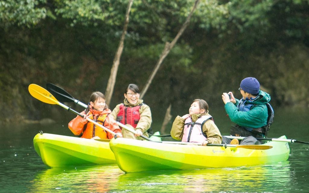 2つのカヌーに乗った家族。父親がカメラで写真を撮り、母親と子供たちがポーズをとっている。