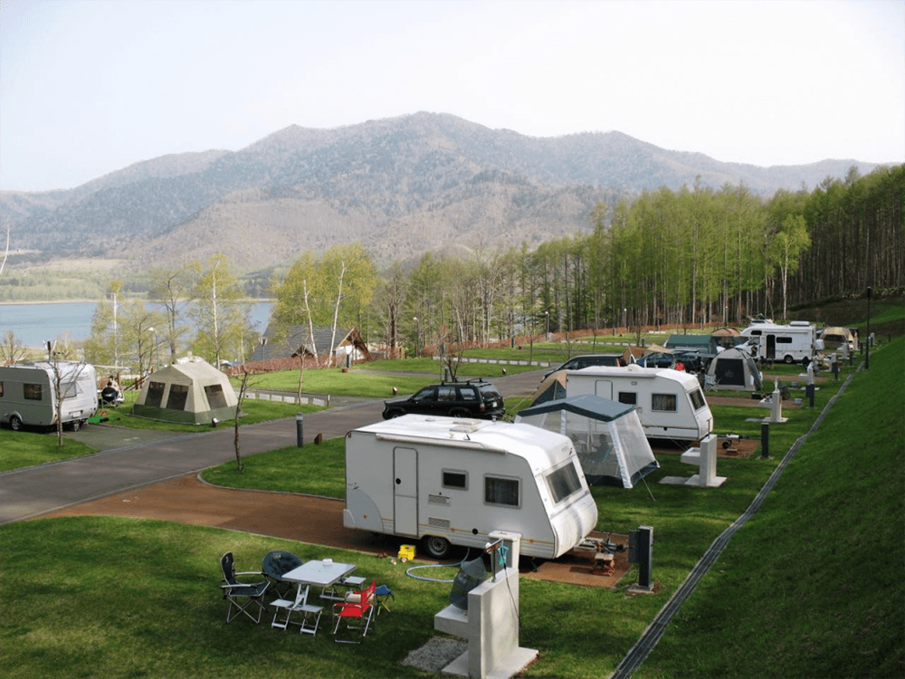 湖のほとりにあるキャンプ場。トレーラーやテントが設置され、向こうには山が見える。