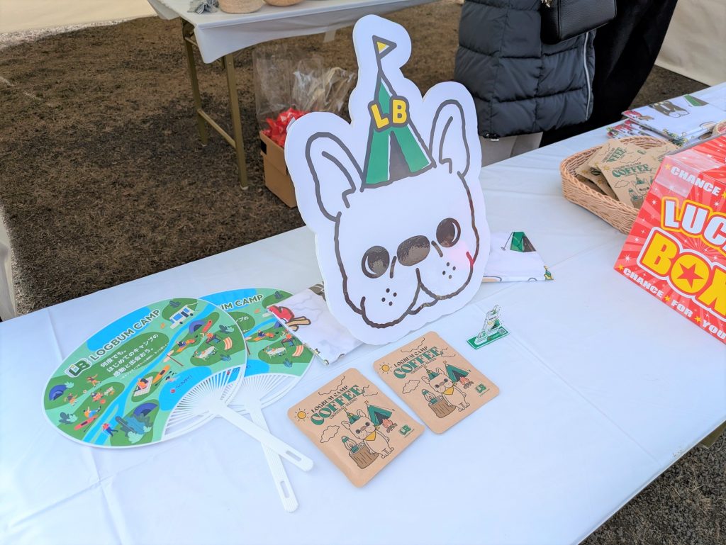 ブースのテーブル。フレンチブルドッグの大きな顔のイラスト、団扇、コーヒーバッグなどの景品が置かれている。