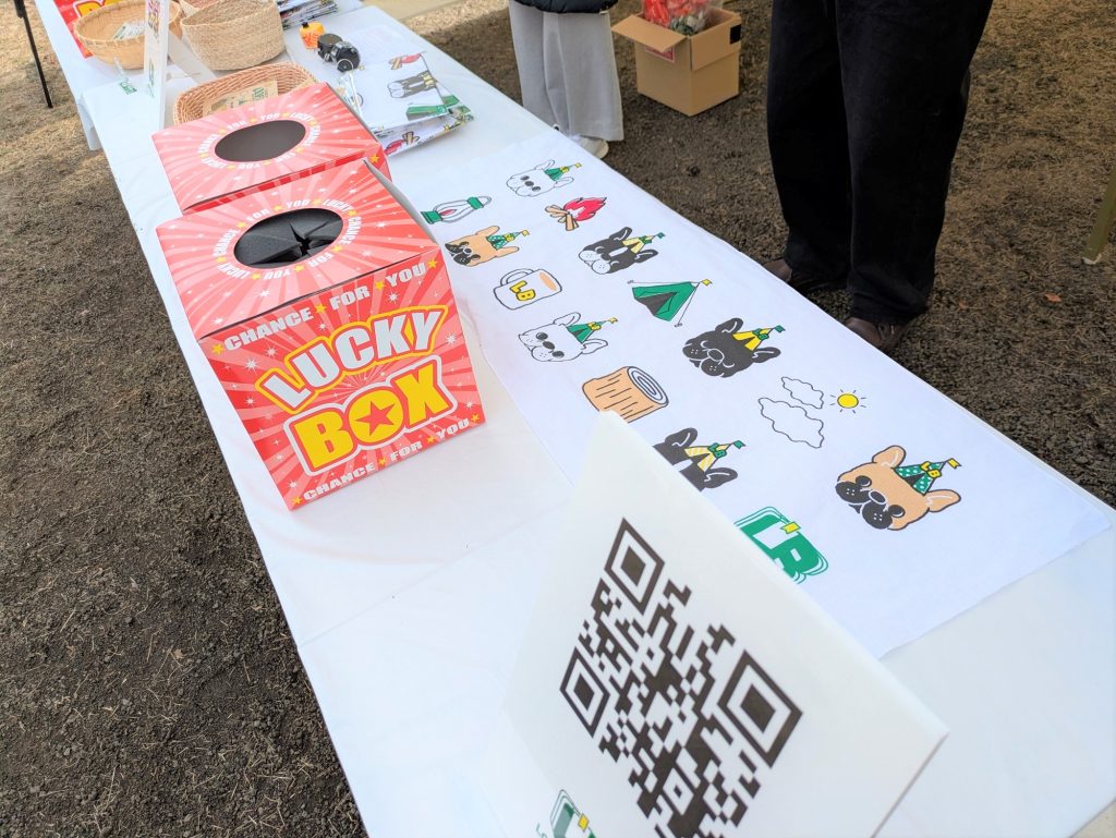 ブースのテーブル。景品と思われる「LUCKY BOX」と書かれた赤い箱と、フレンチブルドッグのイラストが描かれた手ぬぐいが置かれている。