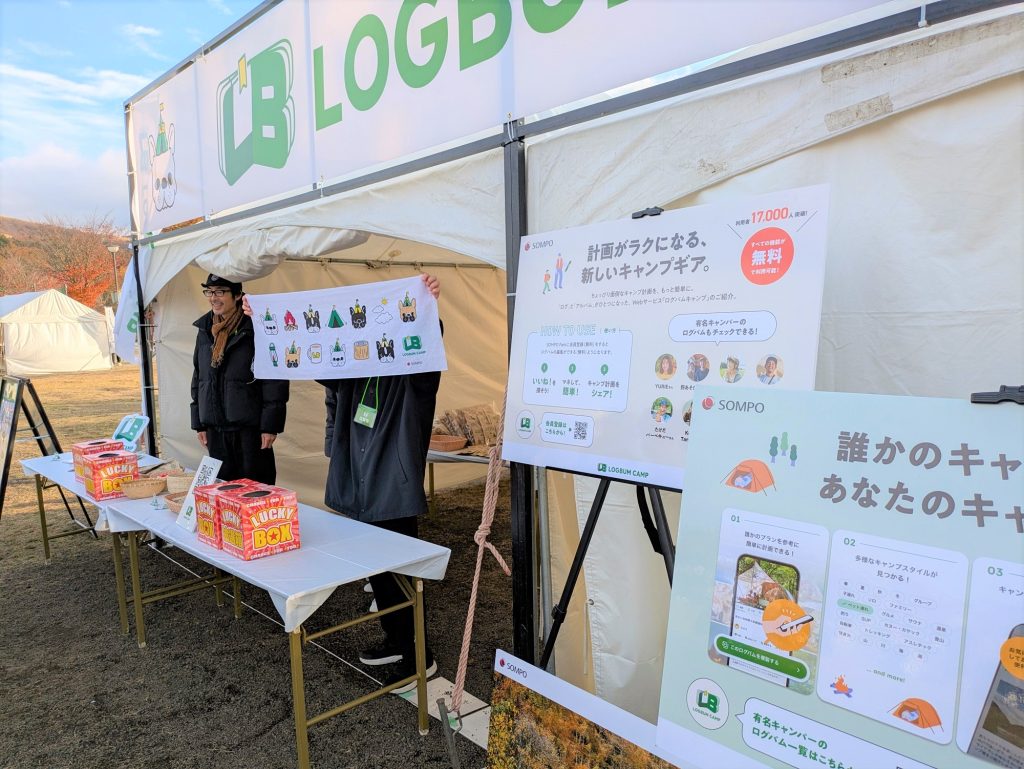 「LOGBUM CAMP」のブース。キャンプに関する説明パネルと、手ぬぐいを持つ人物が立っている。