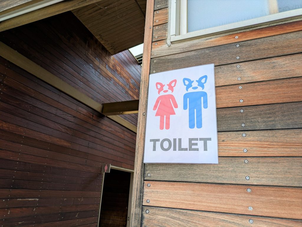 木の壁に貼られたトイレの表示。男女のピクトグラムの頭がフレンチブルドッグの顔になっている。