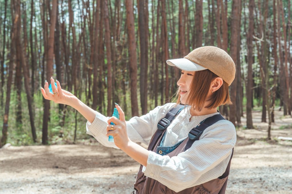 キャンプ場で虫除けスプレー・日焼け止めスプレーを使う女性