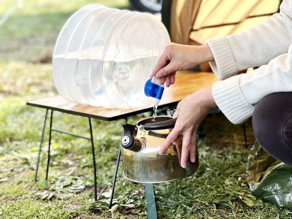 テントでウォータータンクからヤカンに水を入れる女性の手元