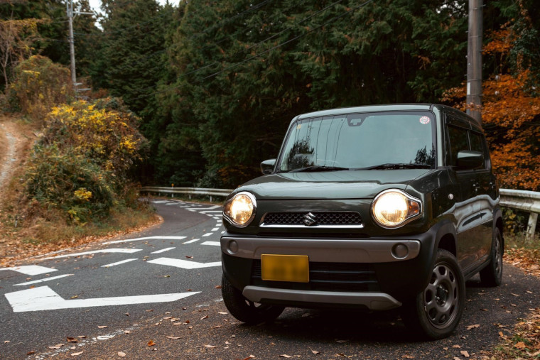 ライトを点灯して山道を走る軽自動車